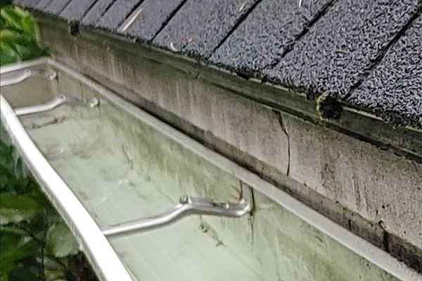 Close-up of clean aluminum gutters attached to a roof in Portland, ME. A crack is visible in the fascia board behind the gutter, indicating potential need for gutter cleaning near me.